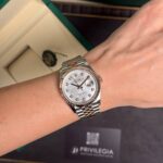 Rolex watch on wrist with a two-tone bracelet and diamond hour markers, in front of green Rolex box.
