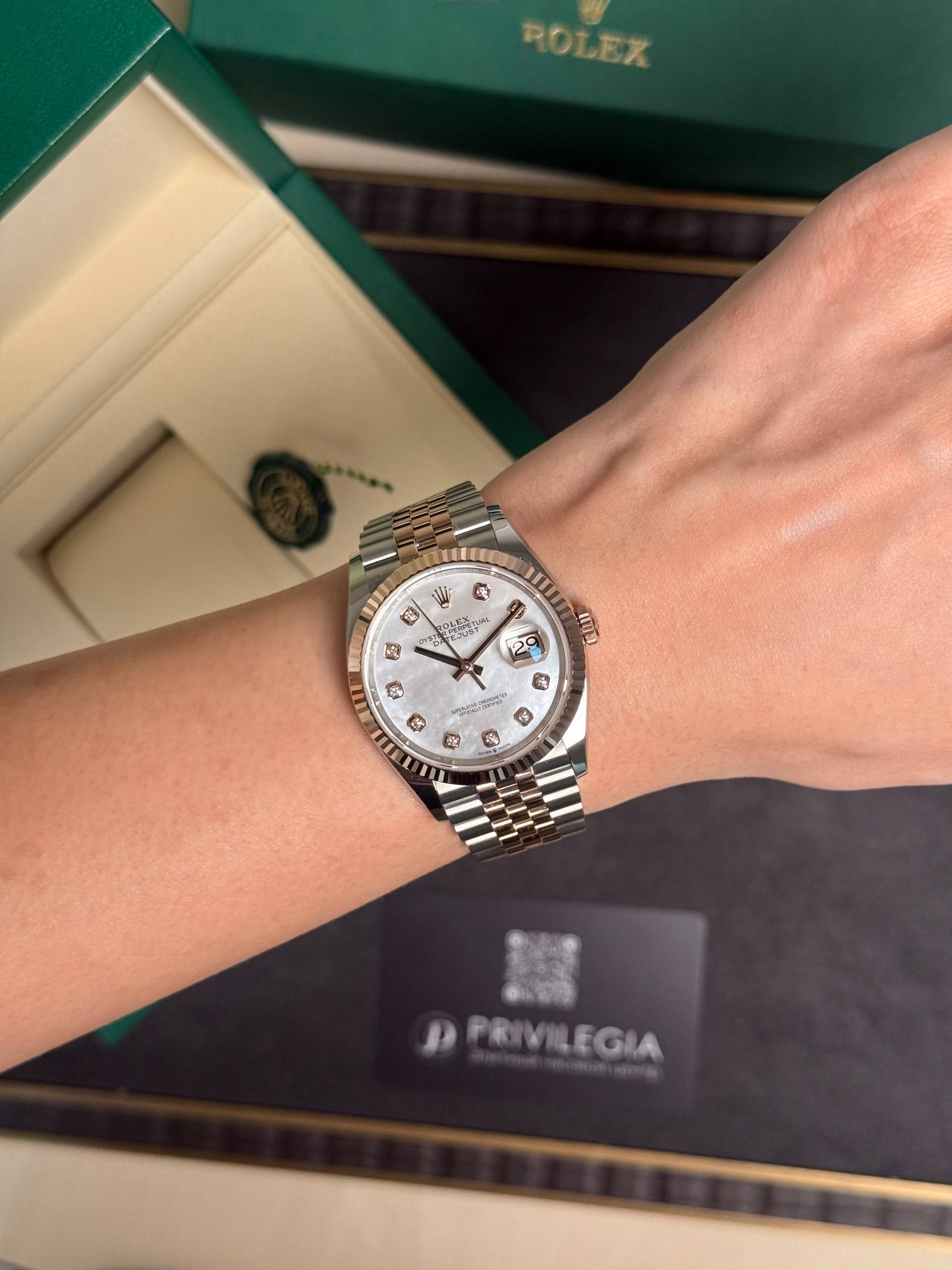 Rolex watch on wrist with a two-tone bracelet and diamond hour markers, in front of green Rolex box.