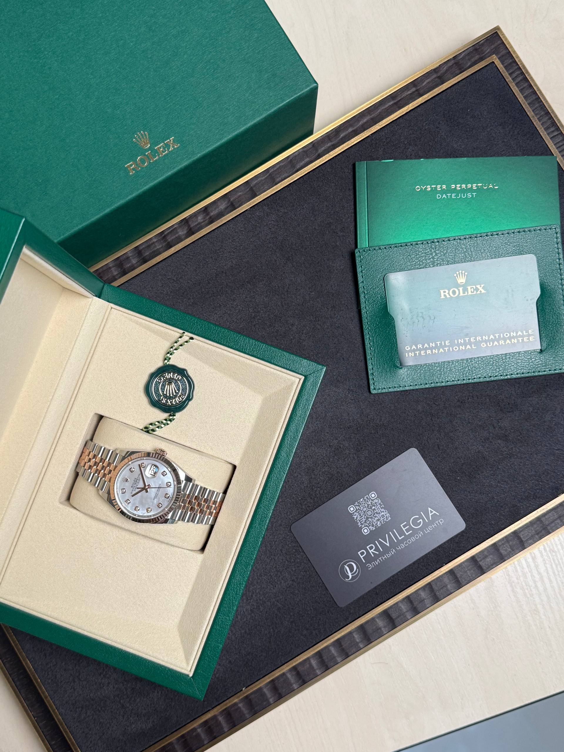 Green Rolex presentation box open to reveal a two-tone metal watch in cream interior with accessories nearby