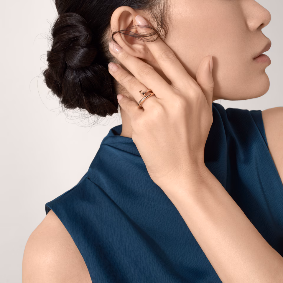 Close-up of a woman with a braided bun, touching her ear while wearing gold rings.