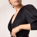Close-up of a woman in a black V-neck dress, showing a rose-gold bracelet on her wrist.