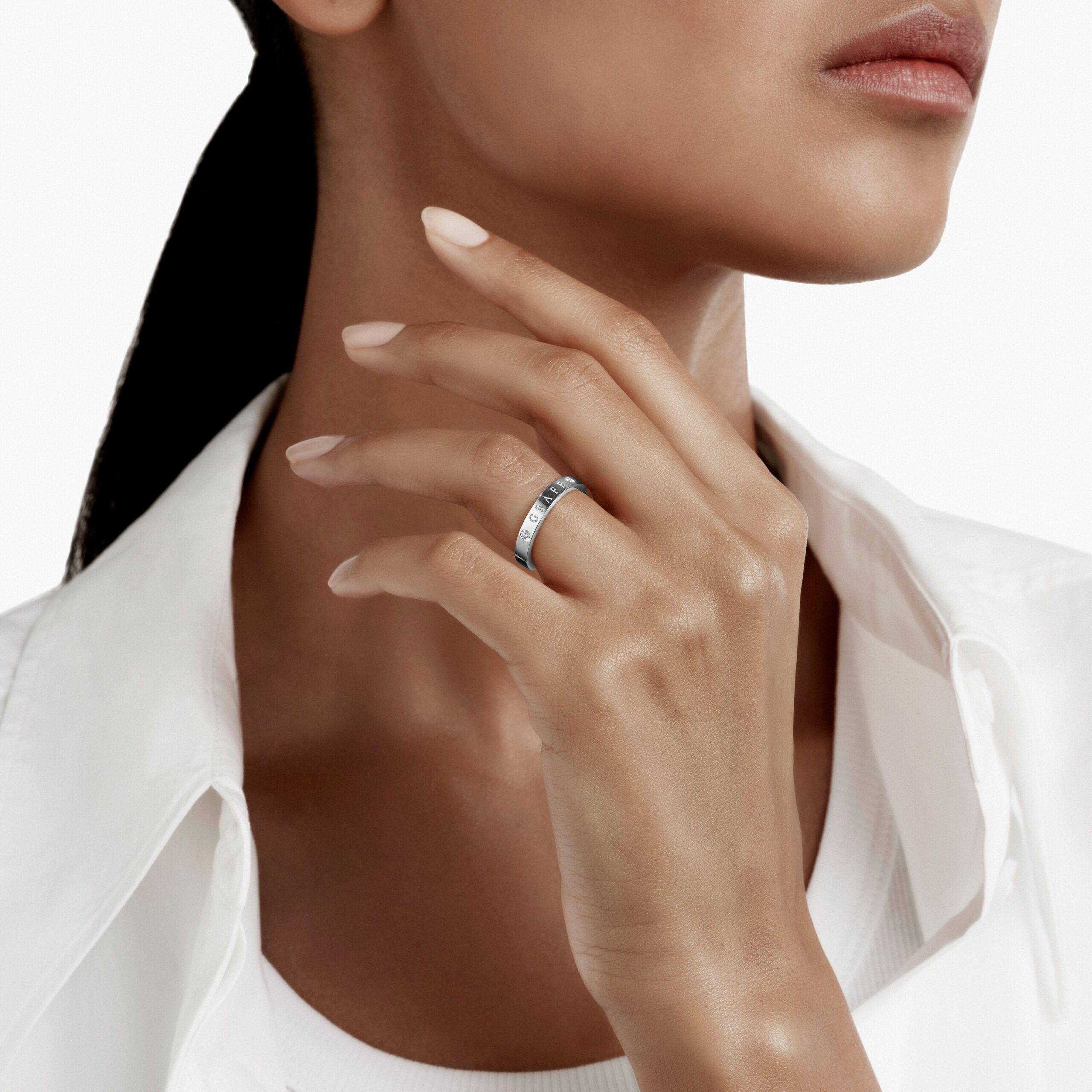 Close-up of a woman’s neck and jaw with a silver ring on her finger resting near her chin, wearing a white shirt.