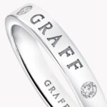 Close-up of a silver ring with a diamond setting and a partially visible engraved word along the band (text reads like 'GRA...').
