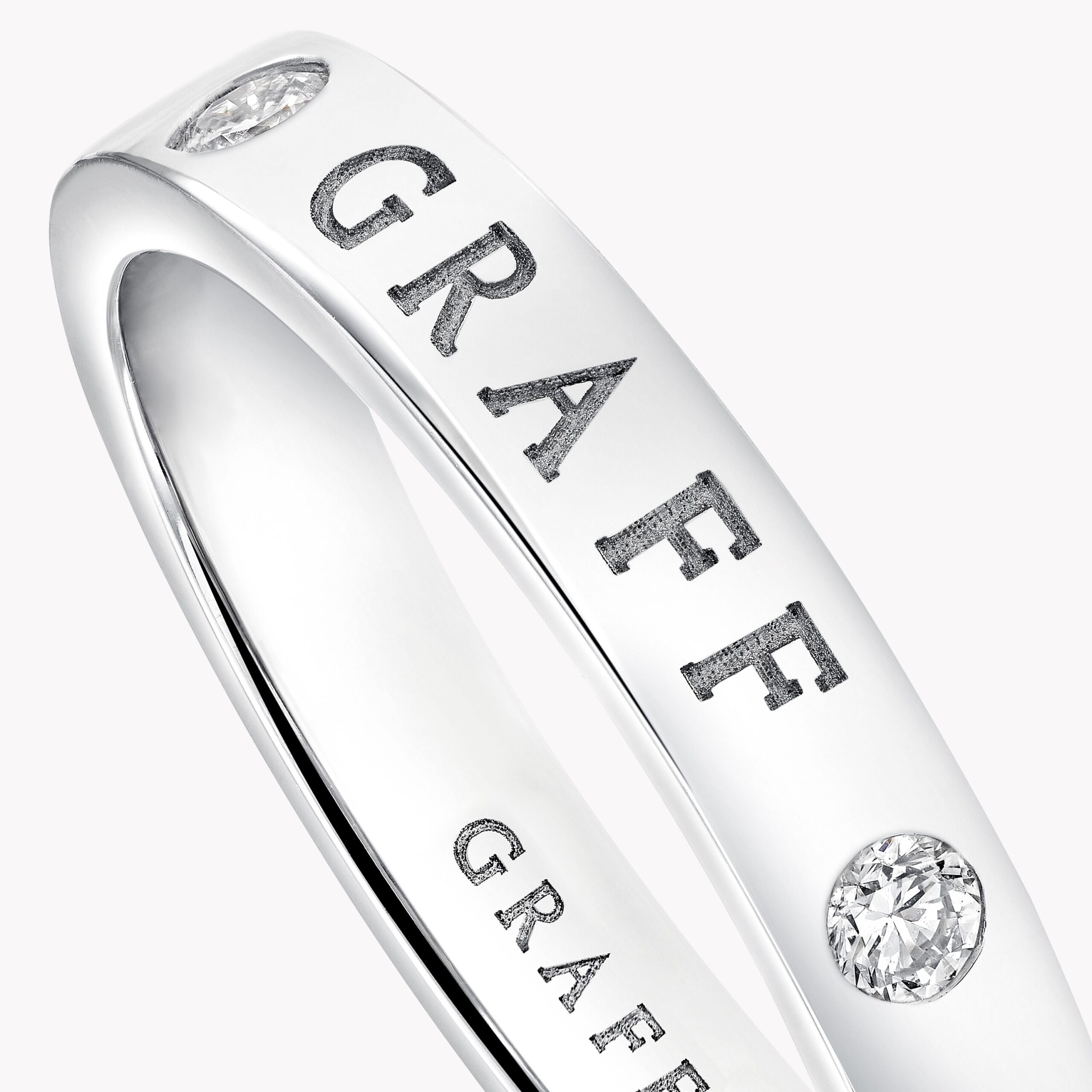 Close-up of a silver ring with a diamond setting and a partially visible engraved word along the band (text reads like 'GRA...').