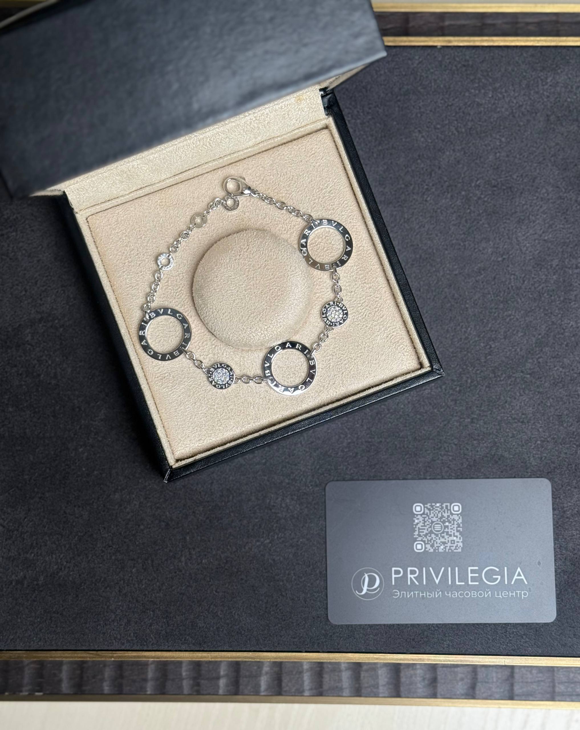 Silver Bulgari bracelet with circular links displayed in a beige jewelry box inside a black case.