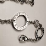 Silver BVLGARI chain bracelet with circular engraved charms on a neutral surface, close-up view.