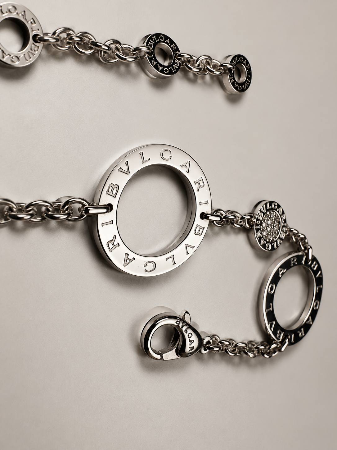 Silver BVLGARI chain bracelet with circular engraved charms on a neutral surface, close-up view.
