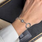 Close-up of a silver Bulgari bracelet worn on the wrist, showing circular charms and engraved text.