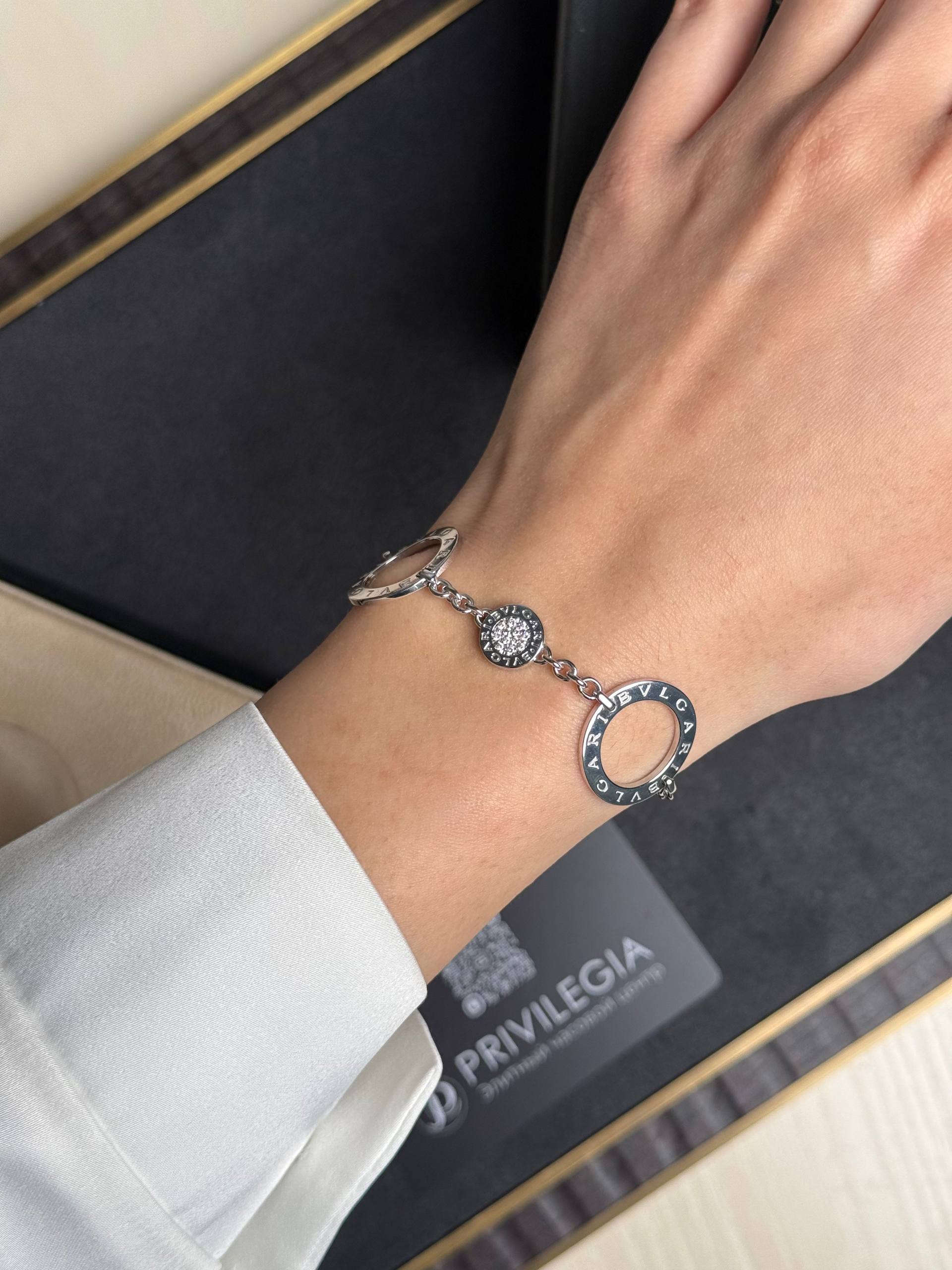 Close-up of a silver Bulgari bracelet worn on the wrist, showing circular charms and engraved text.
