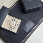 Black BVLGARI jewelry box opened to reveal a silver bracelet in a beige insert, with a BVLGARI card nearby