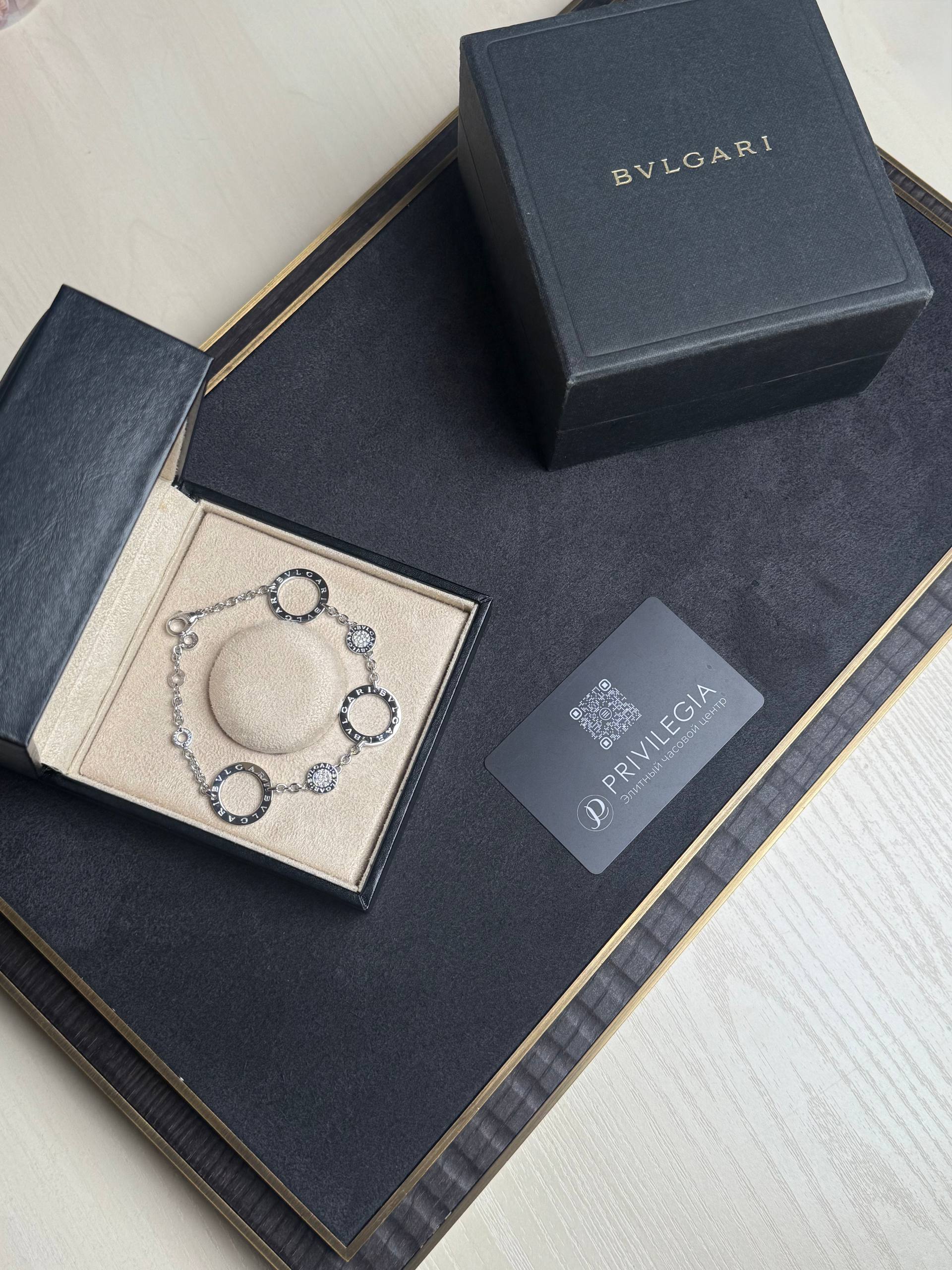 Black BVLGARI jewelry box opened to reveal a silver bracelet in a beige insert, with a BVLGARI card nearby