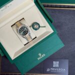 Open green Rolex presentation box revealing a two-tone Rolex watch with diamond bezel and a green seal tag.
