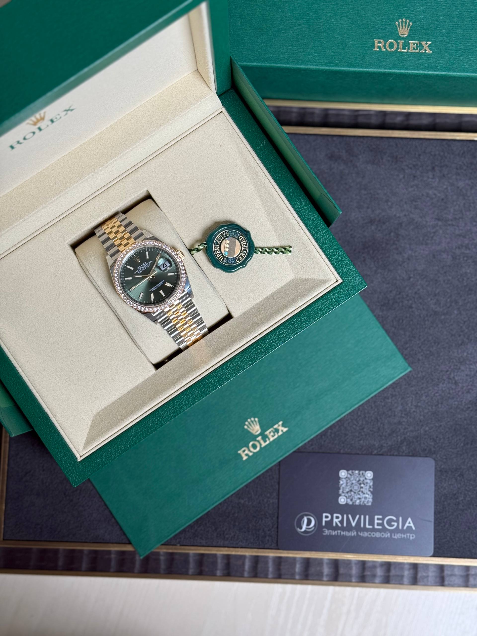 Open green Rolex presentation box revealing a two-tone Rolex watch with diamond bezel and a green seal tag.