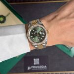 Rolex Oyster Perpetual Datejust with green dial and diamond bezel worn on a wrist with a two-tone bracelet in a presentation box.
