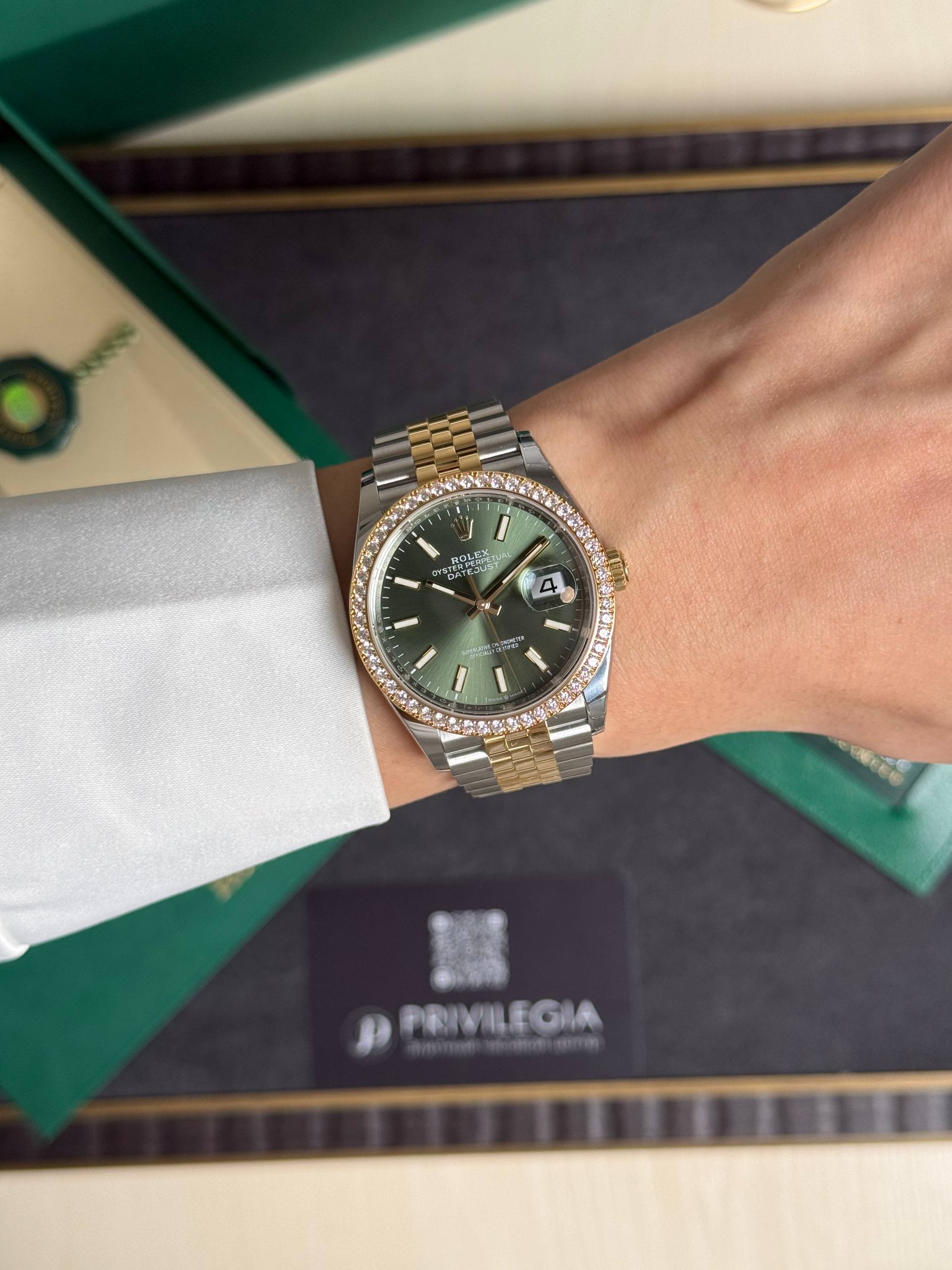 Rolex Oyster Perpetual Datejust with green dial and diamond bezel worn on a wrist with a two-tone bracelet in a presentation box.