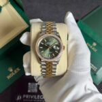 Two-tone Rolex Datejust with green dial and diamond bezel held in white gloves on a display cushion