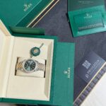 Green Rolex presentation box with watch nestled in a cream inner case and accompanying green warranty cards and tags laid out nearby.