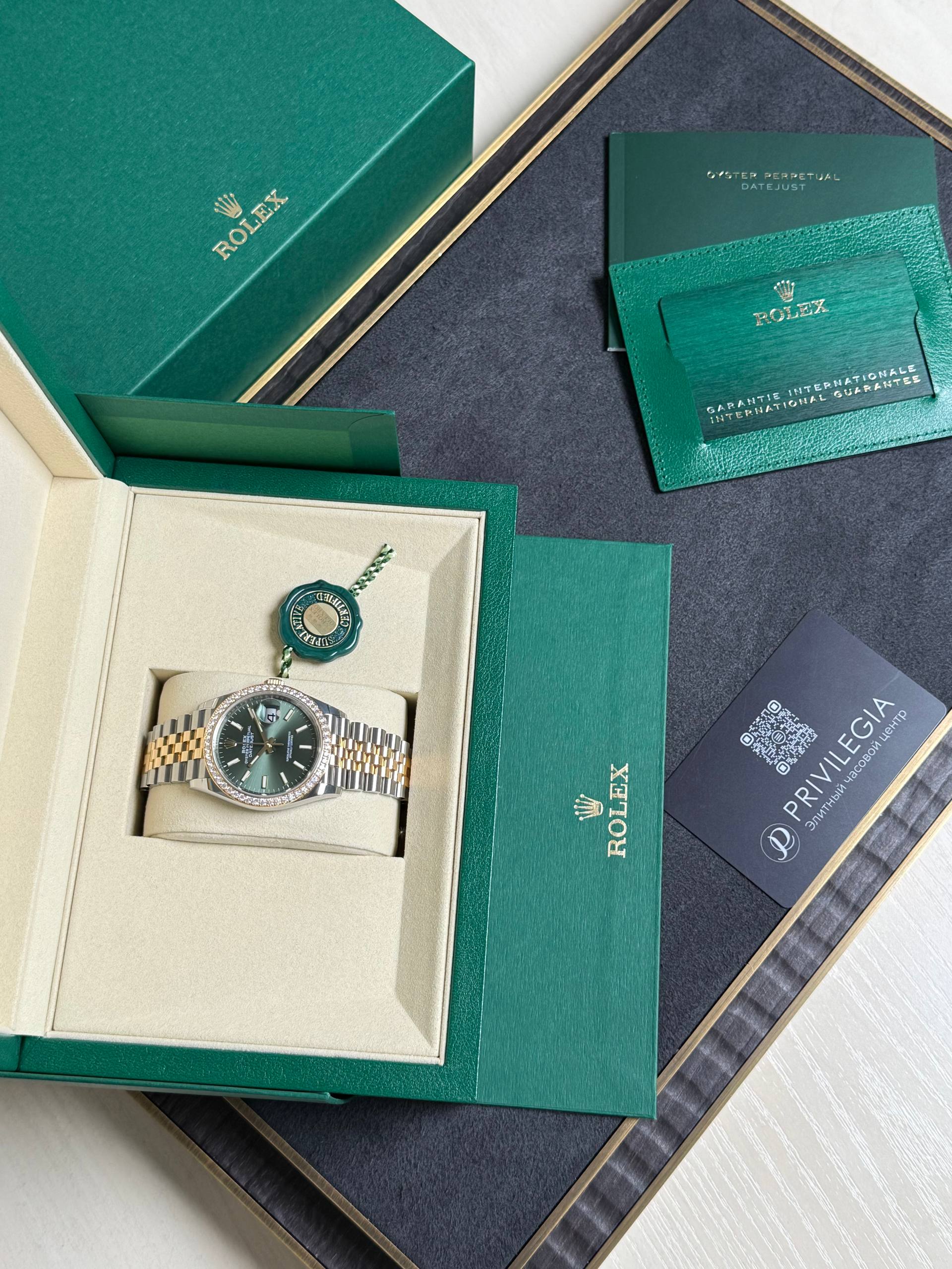 Green Rolex presentation box with watch nestled in a cream inner case and accompanying green warranty cards and tags laid out nearby.