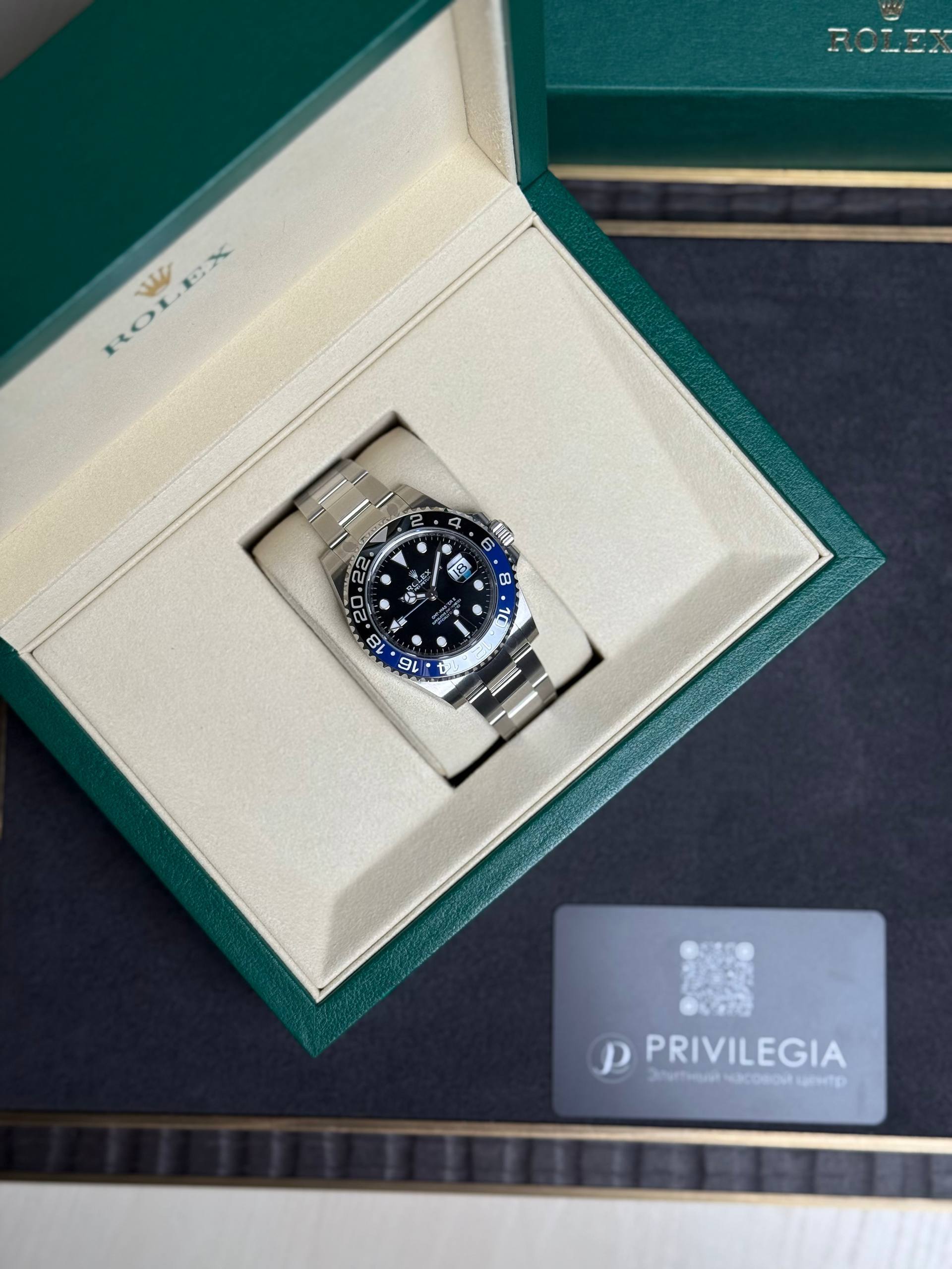 Rolex watch in an open green presentation box with beige interior, showing a stainless steel bracelet and dark dial with date window; Privilegia card nearby.