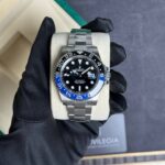 Close-up of a stainless steel Rolex GMT-Master II watch with a blue-black bi-color bezel, held in a gloved hand over a beige cushion.