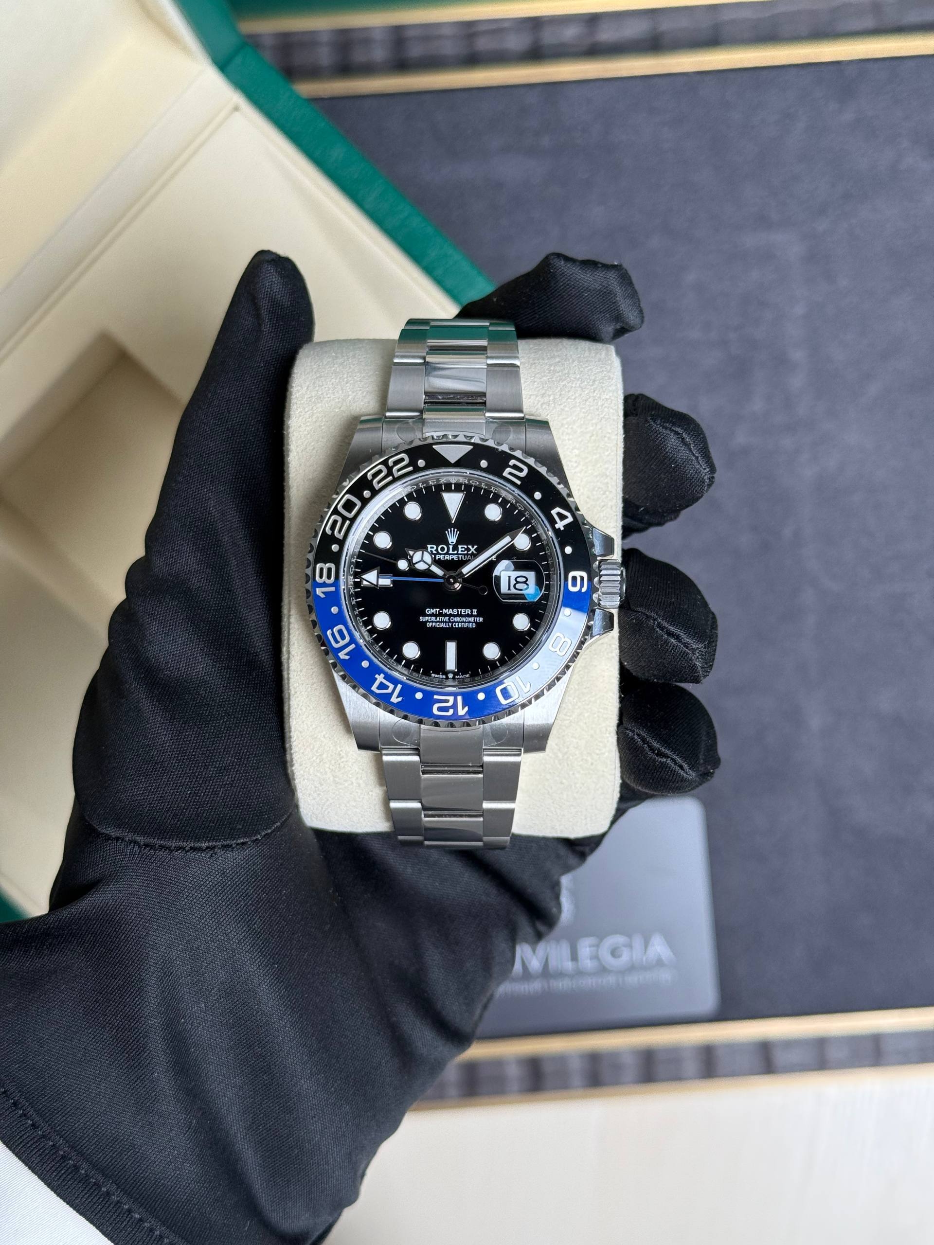 Close-up of a stainless steel Rolex GMT-Master II watch with a blue-black bi-color bezel, held in a gloved hand over a beige cushion.
