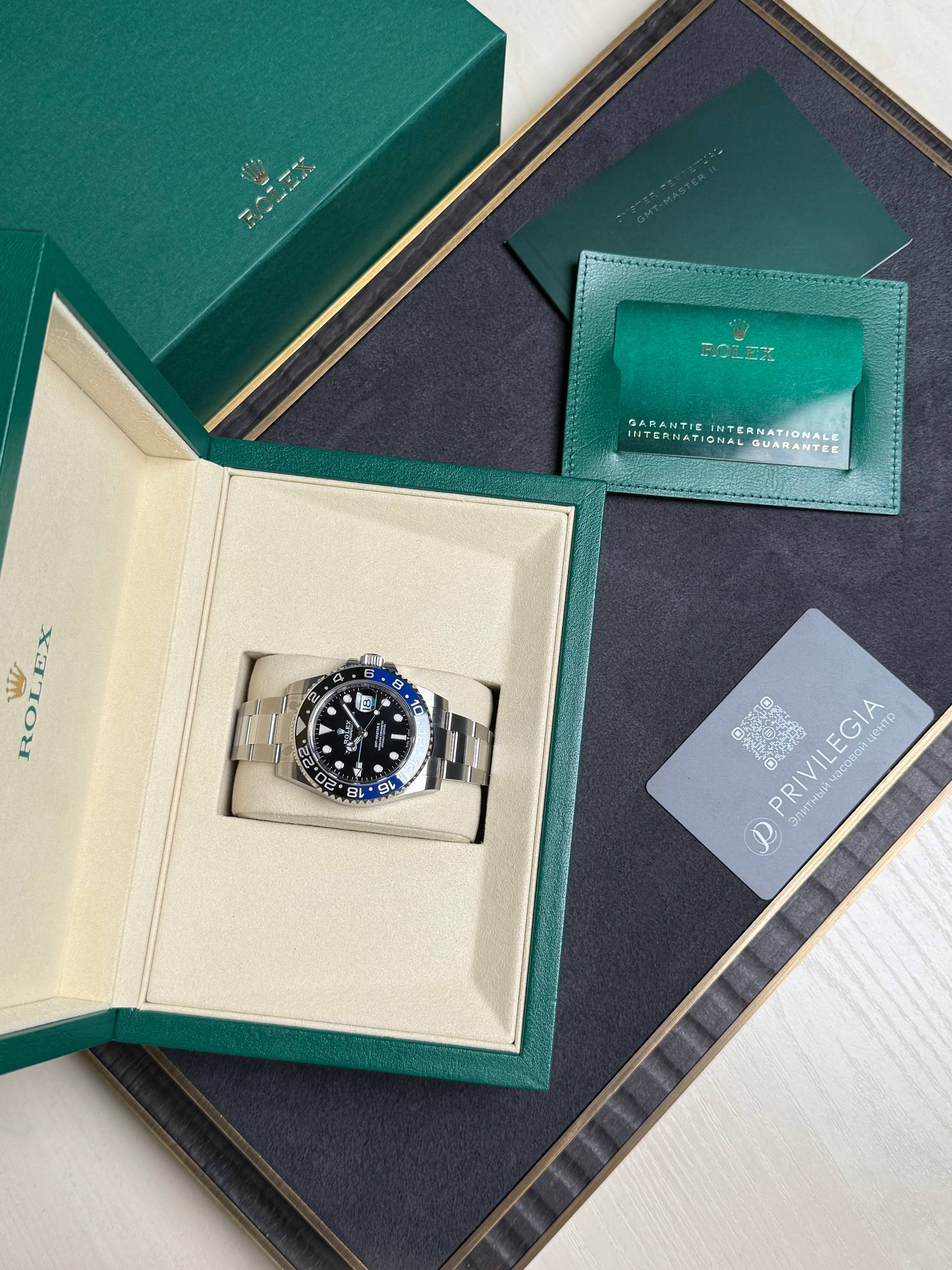 Rolex watch in an open beige interior box with green outer case and accompanying warranty cards and papers nearby.