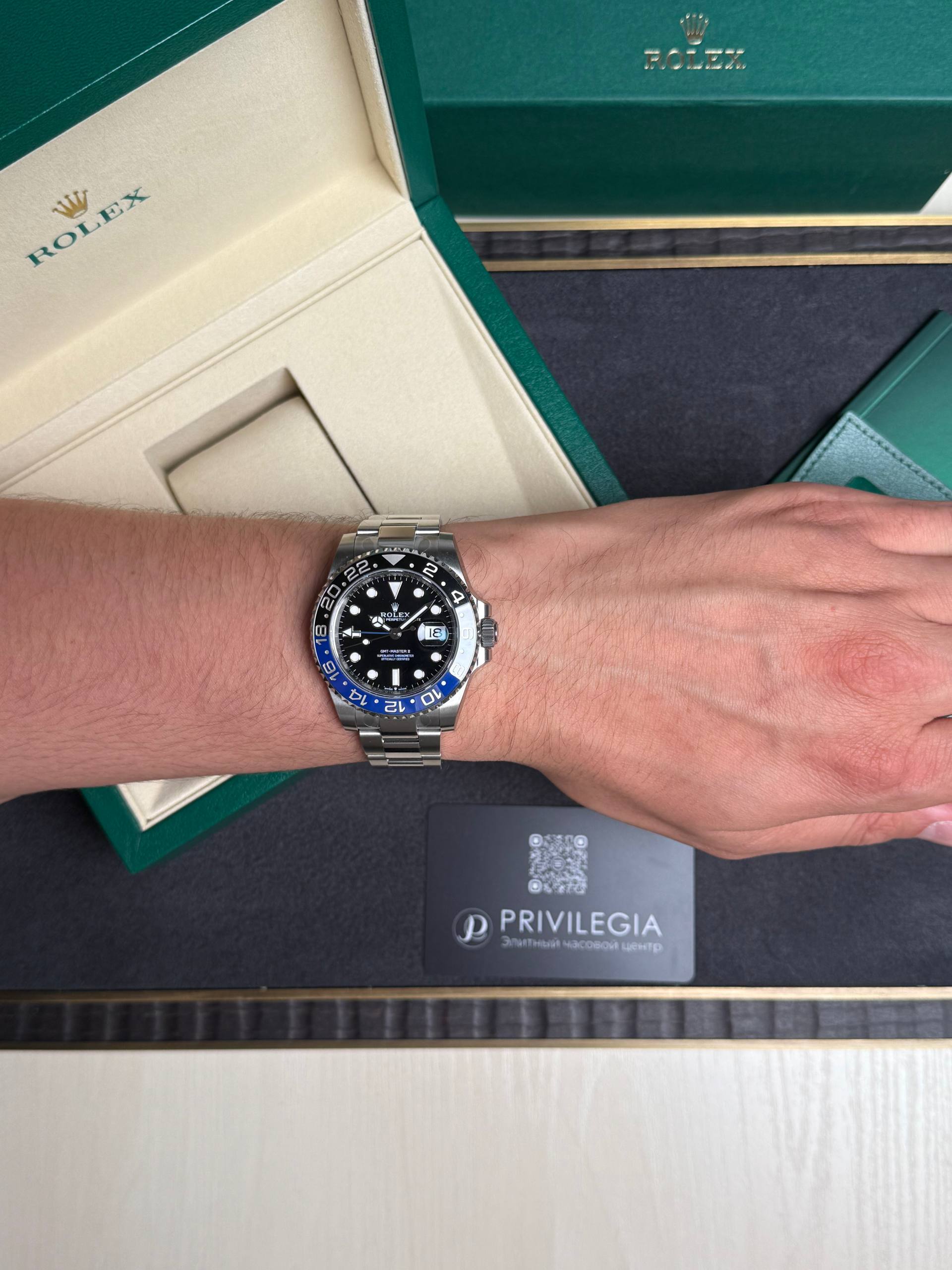 Wrist wearing a stainless steel Rolex GMT-Master II with blue/black bezel, open green Rolex box in the background.