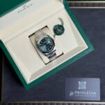 Rolex watch in an open green box with a cream interior, green seal tag nearby.
