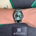 Wrist wearing a stainless steel Rolex with green dial and date window on the bracelet roll hubbing a dark surface.