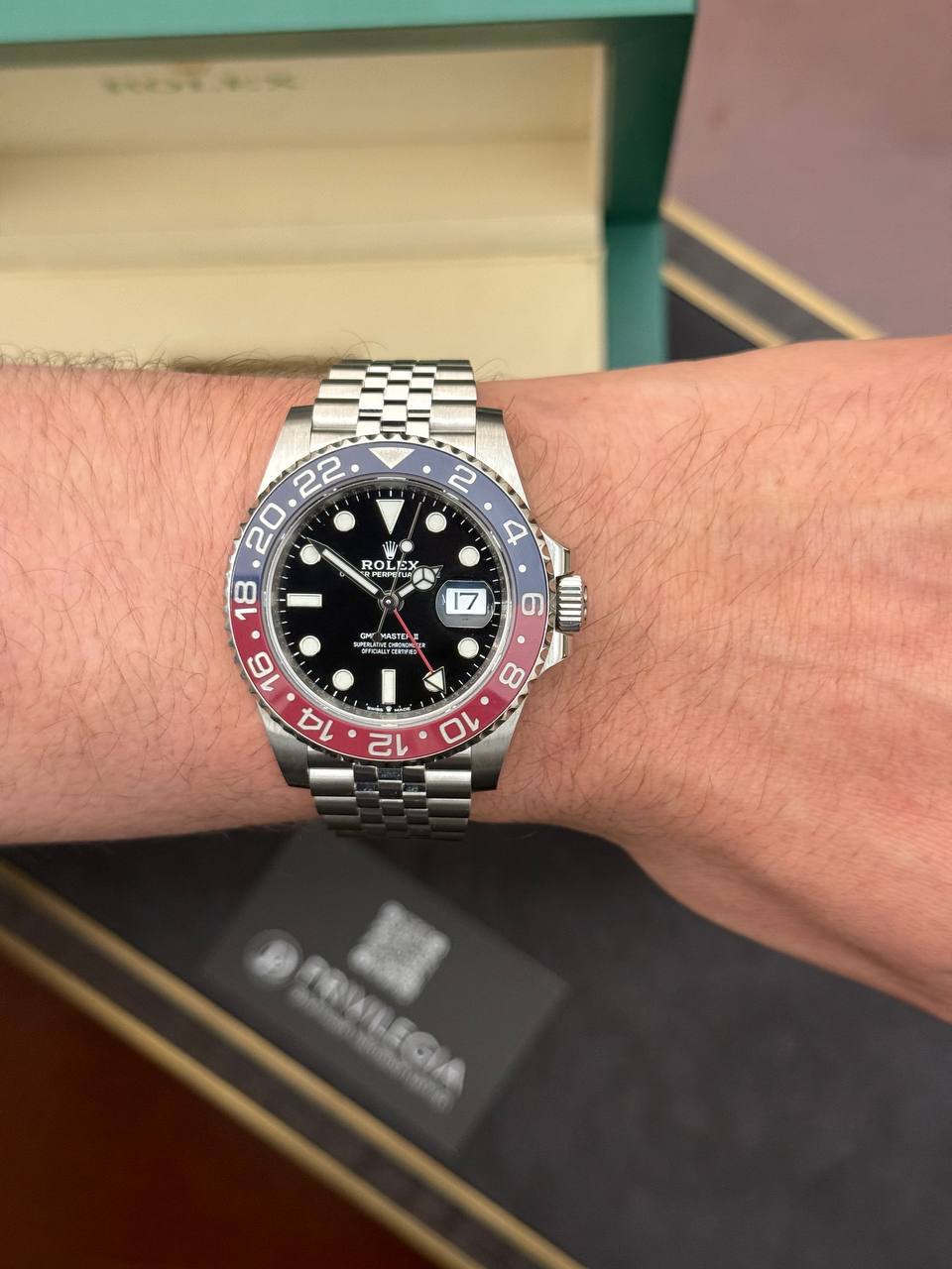 Rolex GMT-Master II with a red/blue bezel on a metal Jubilee bracelet worn on the left wrist; black dial with date magnifier.