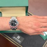 Wrist shot of a stainless steel Rolex GMT-Master II with a red‑blue bezel, worn on the left wrist, with a green box in the background.