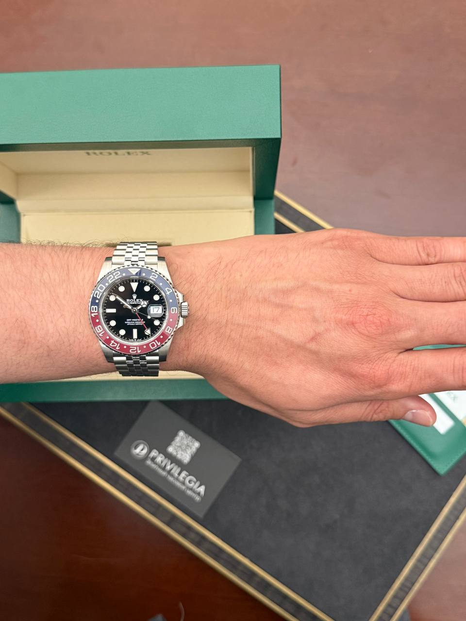 Wrist shot of a stainless steel Rolex GMT-Master II with a red‑blue bezel, worn on the left wrist, with a green box in the background.