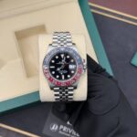 Rolex GMT-Master II with black dial, red/blue bezel, and Jubilee bracelet held by a gloved hand in a beige presentation box.
