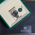 Rolex wristwatch in a beige interior box with a green outer lid and a green seal tag beside it, plus a Privilegia card nearby.