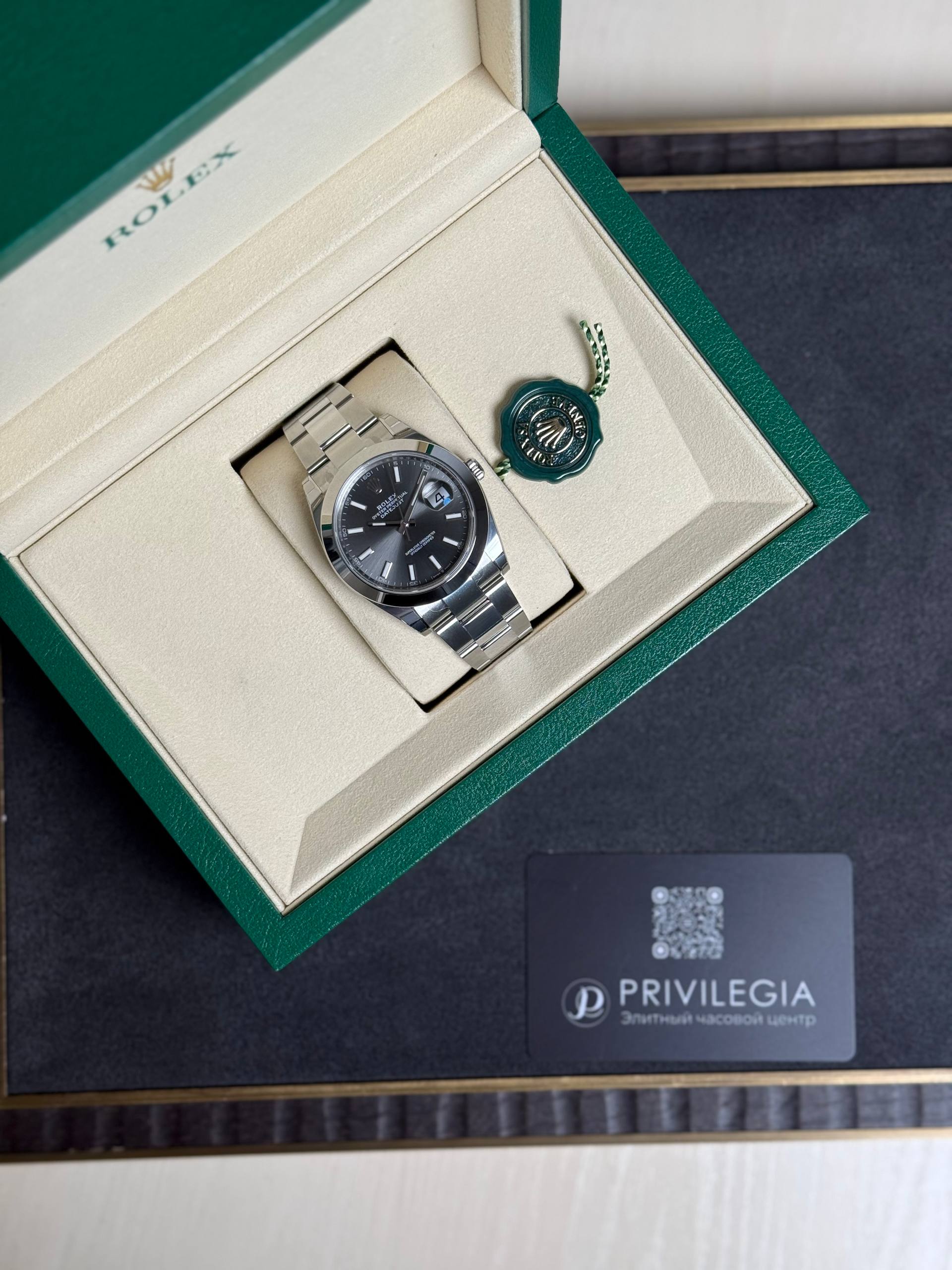 Rolex wristwatch in a beige interior box with a green outer lid and a green seal tag beside it, plus a Privilegia card nearby.
