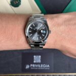 Close-up of a silver Rolex Datejust on a man's wrist, showing the dark dial and date window at 3 o'clock