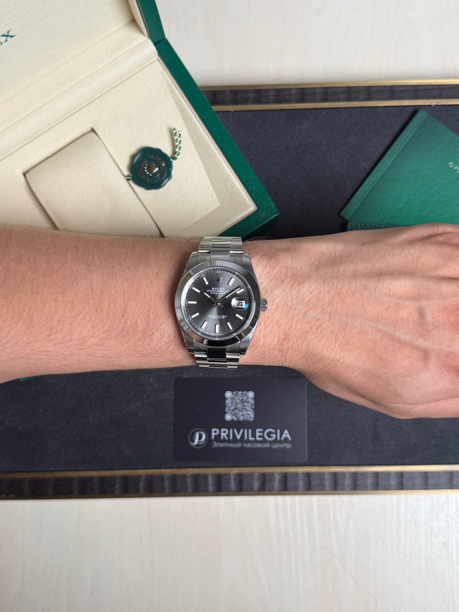 Silver Rolex watch on a forearm, with green Rolex box, green booklet, and a Privilegia card visible in the background.