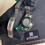 Close-up of stainless steel wristwatch on a gloved hand, showing the case back and linked bracelet in a display box.