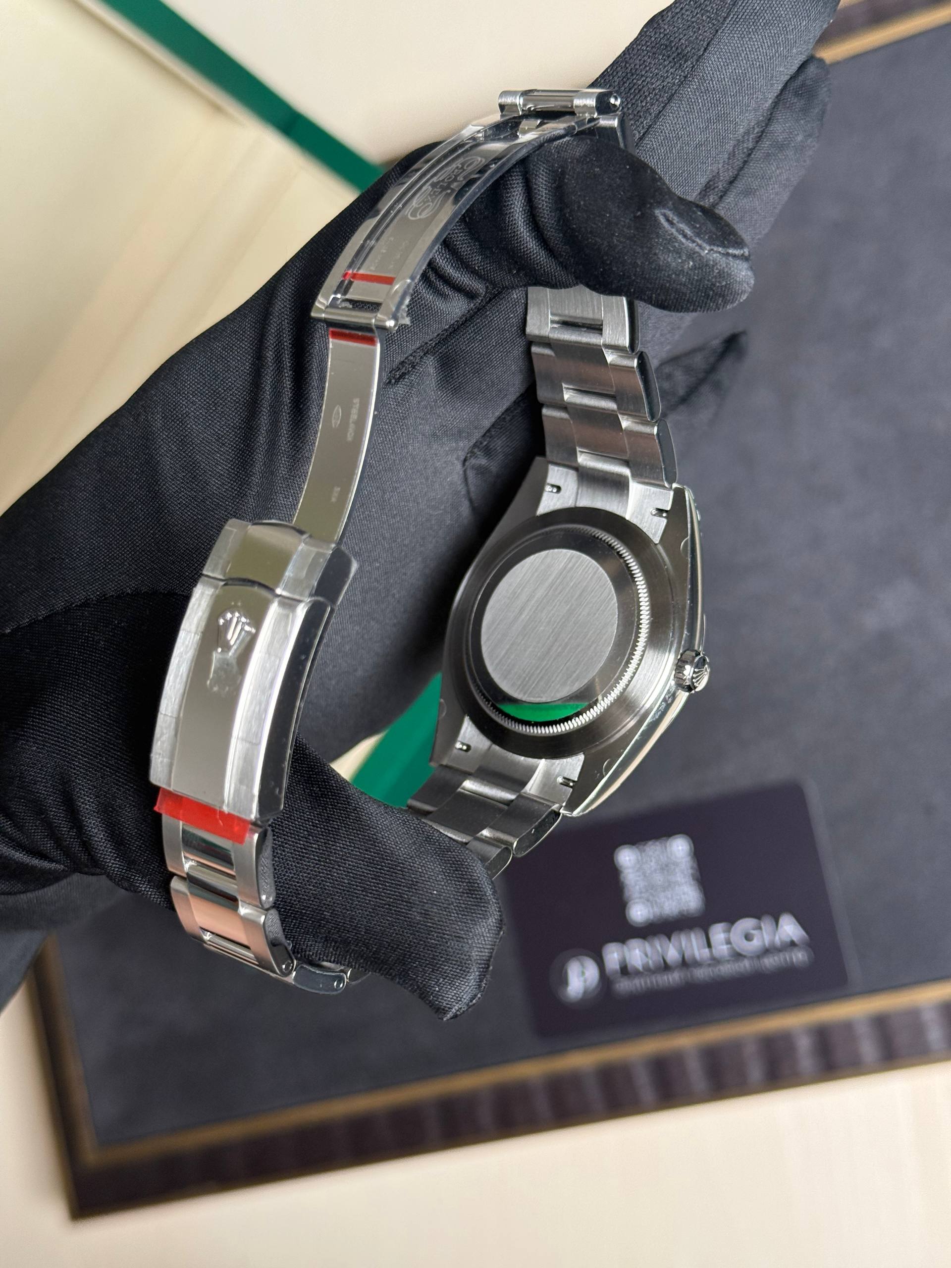 Close-up of stainless steel wristwatch on a gloved hand, showing the case back and linked bracelet in a display box.