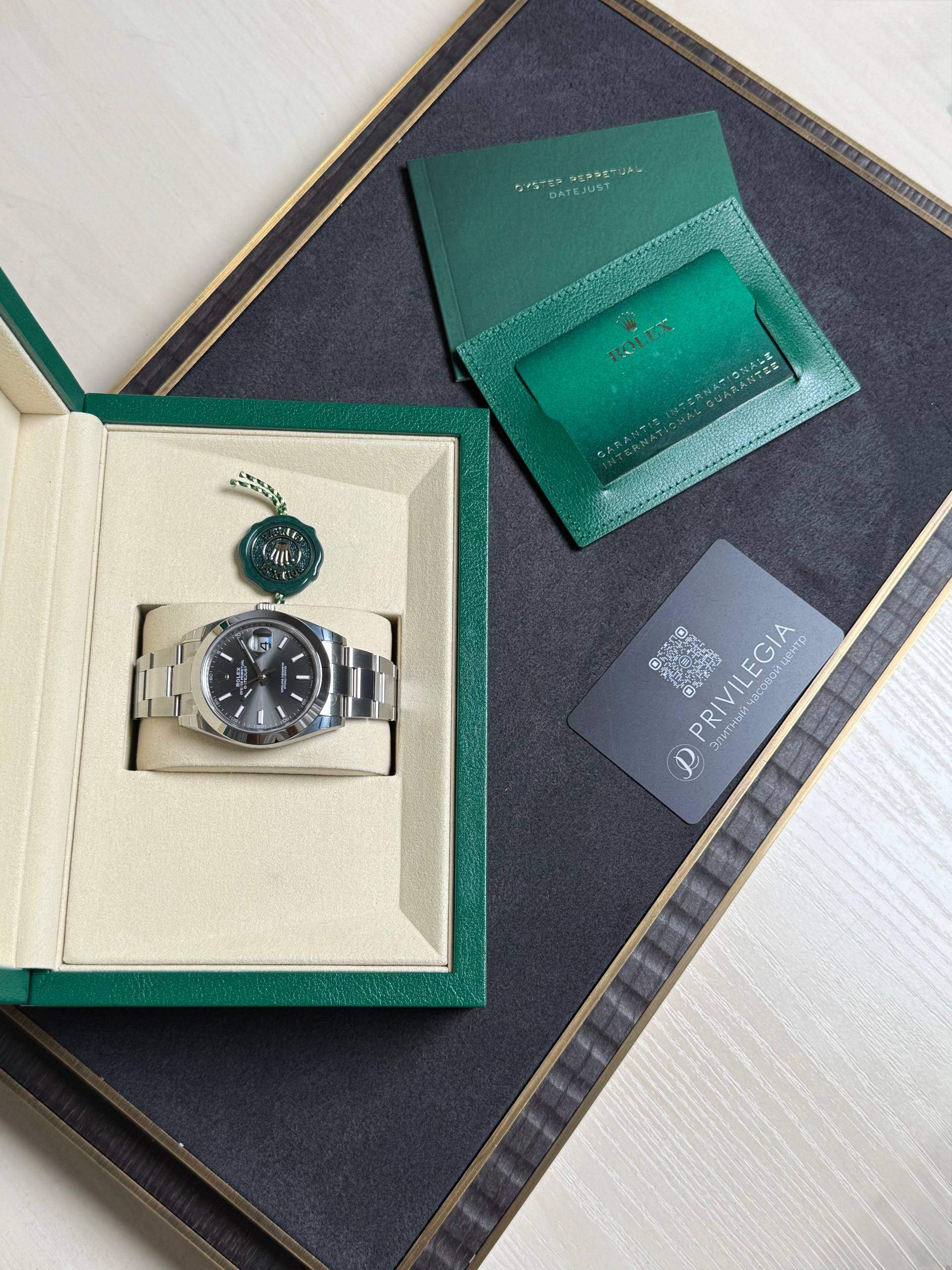 Rolex watch displayed in a beige insert inside a green presentation box, with a green warranty card and booklet nearby.