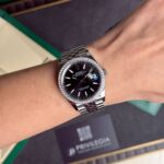 Wrist wearing a Rolex Datejust with a diamond-encrusted bezel and black dial, bracelet visible