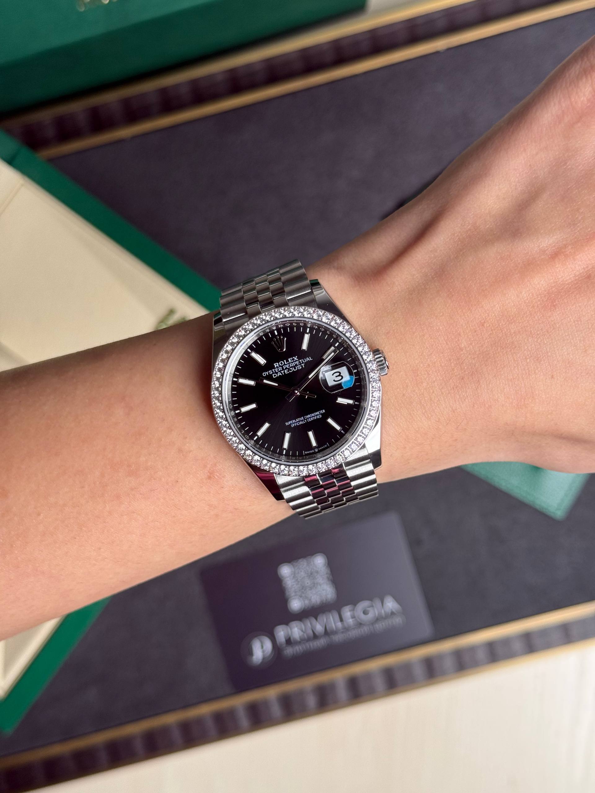 Wrist wearing a Rolex Datejust with a diamond-encrusted bezel and black dial, bracelet visible