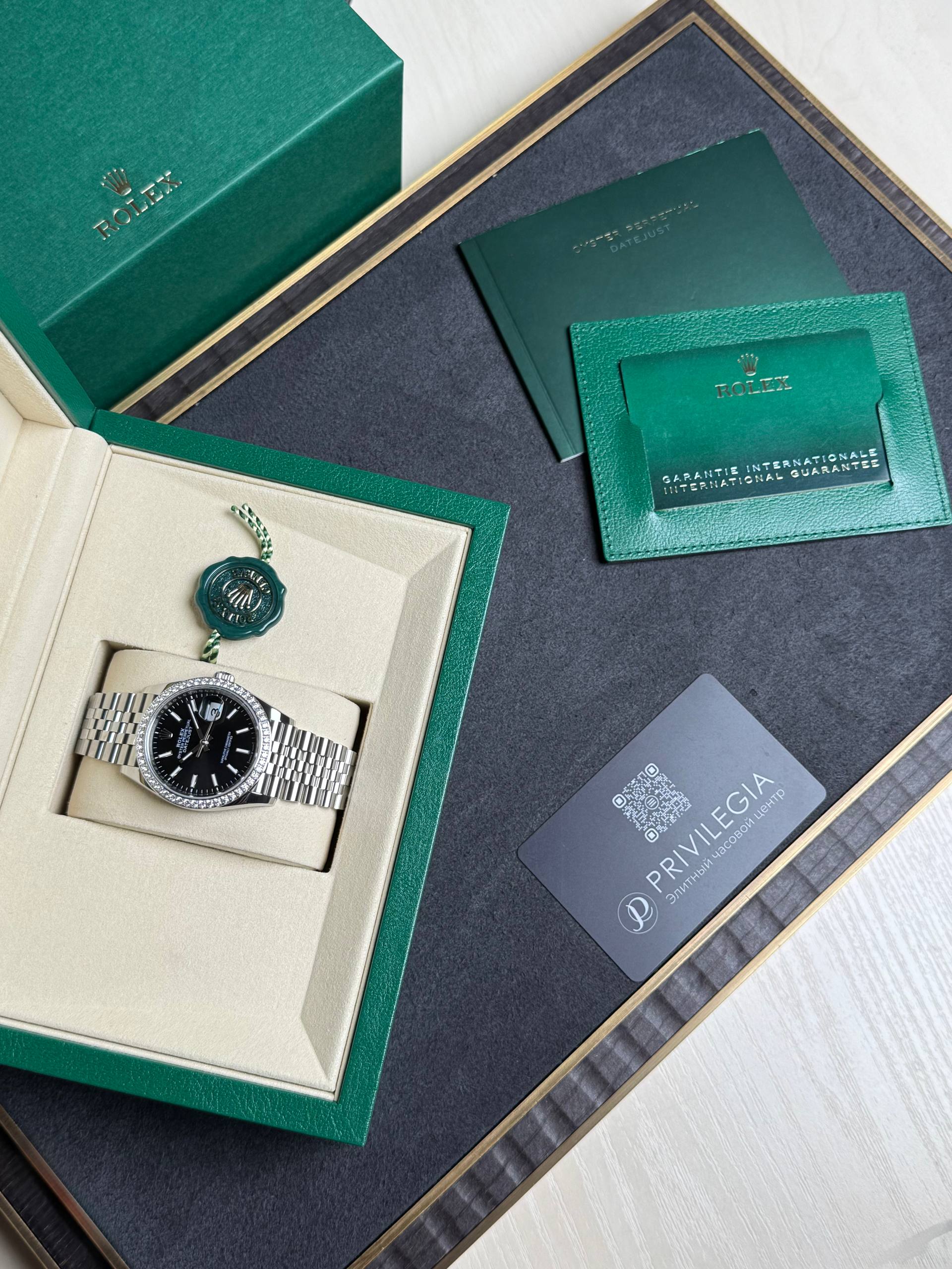 Rolex watch in a beige display box inside a green presentation box, with a green warranty card and documents nearby.