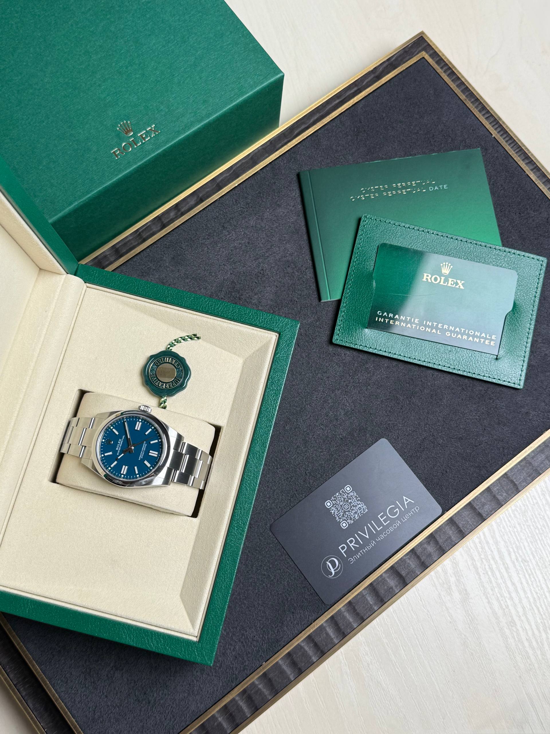 Rolex watch displayed in a beige insert inside a green box, with green warranty cards nearby much of the packaging visible.