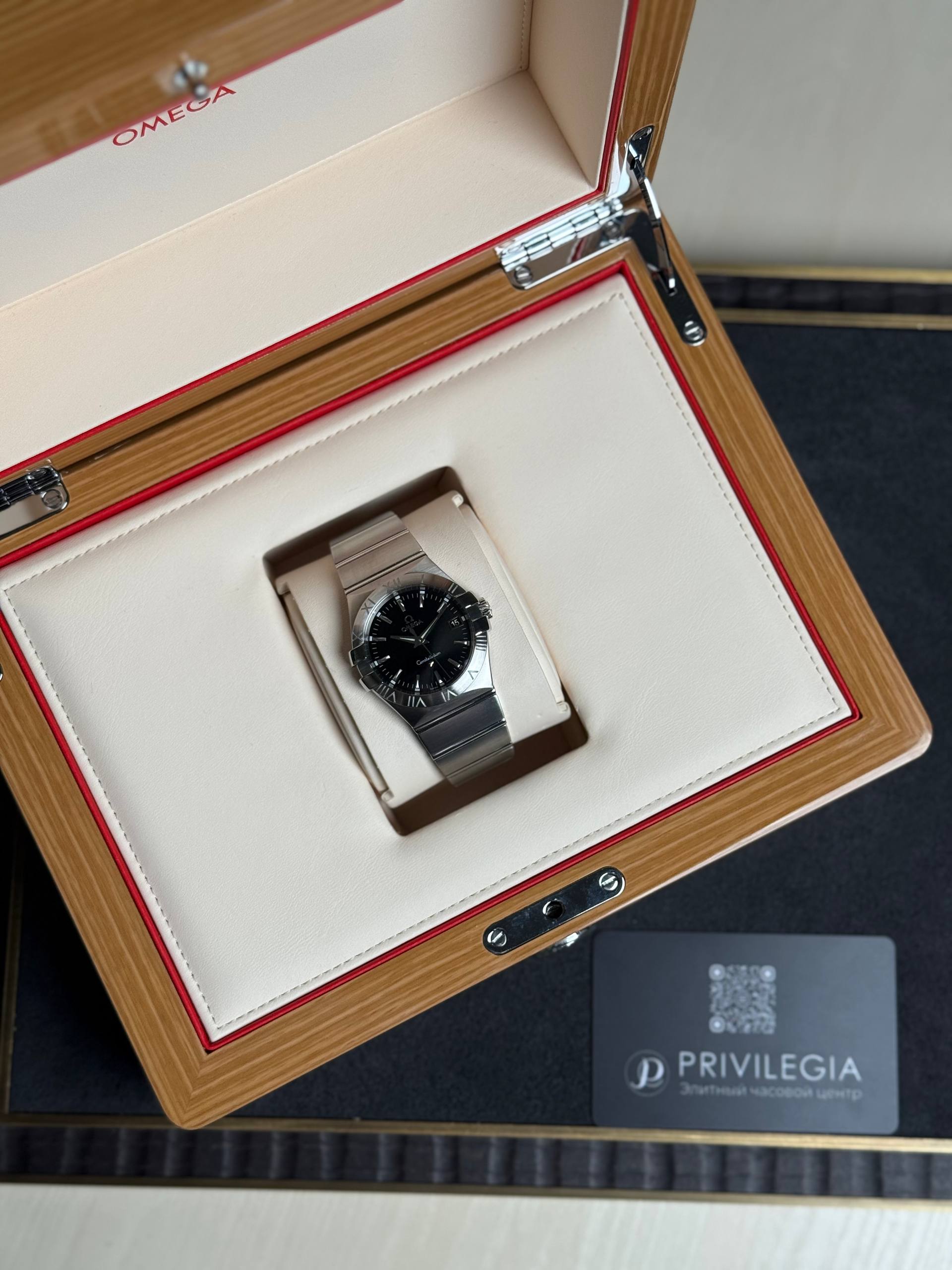 Omega watch in an open wooden box with cream interior and red trim, Privilegia card nearby