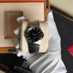 Omega Constellation wristwatch in a light beige display box with white gloves holding it, close-up view.