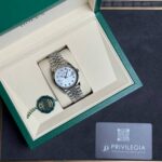 Rolex watch in its green presentation box with a beige interior, green seal, and Privilegia card on a dark surface.