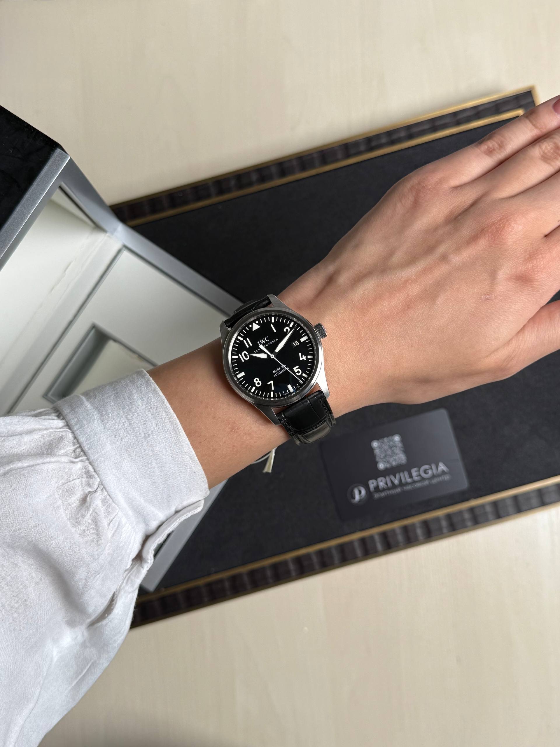 Wrist wearing a black IWC pilot watch with a leather strap resting near a watch presentation box.