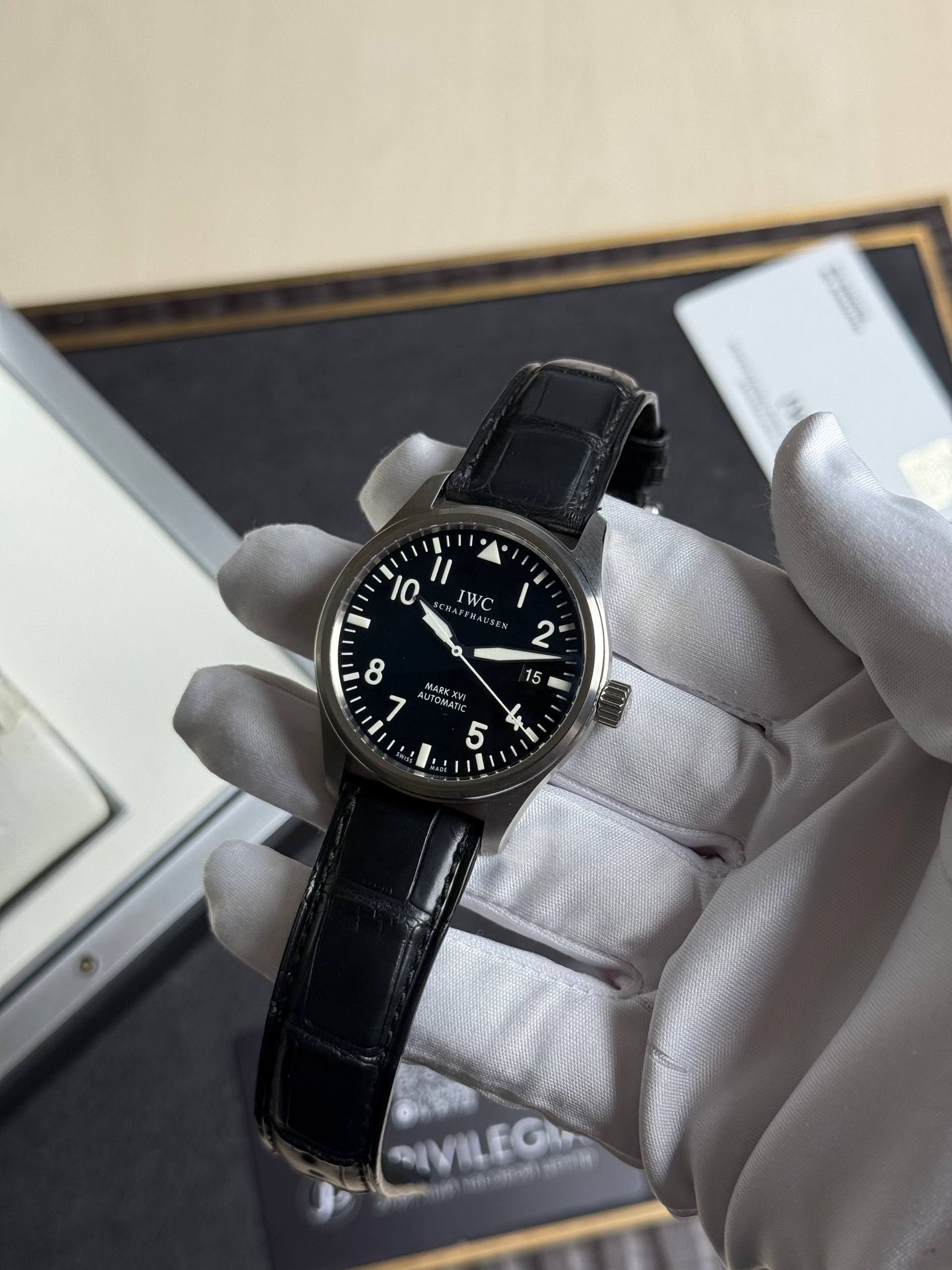 Close-up of an IWC pilot watch with a black dial and leather strap held by a gloved hand.