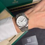 Stainless steel Rolex watch with a fluted bezel and date window worn on the wrist, with a green Rolex box in the background.